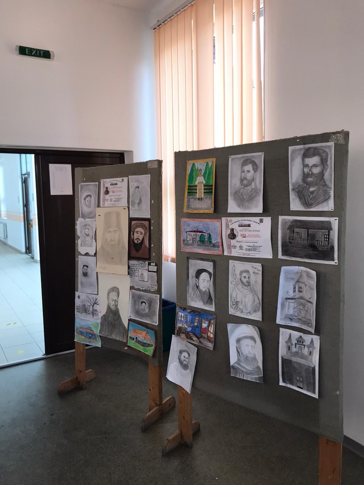 Expoziție de desene ale elevilor pe holul școlii: portrete și case tradiționale